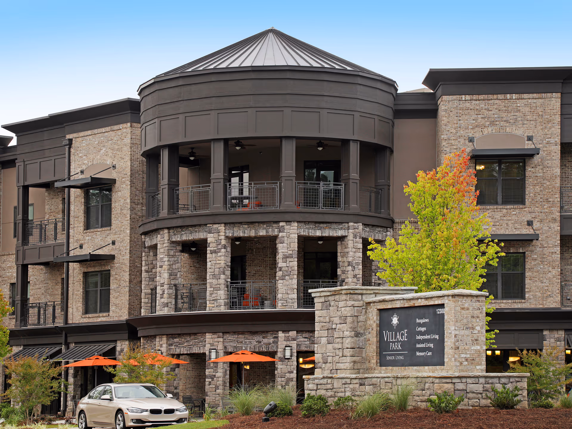 Exterior view of Village Park Alpharetta senior living building with signage and parked car.