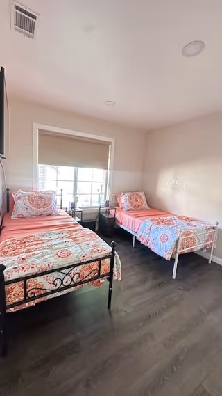 Two twin beds with pink patterned bedding in a bright, minimalist bedroom.