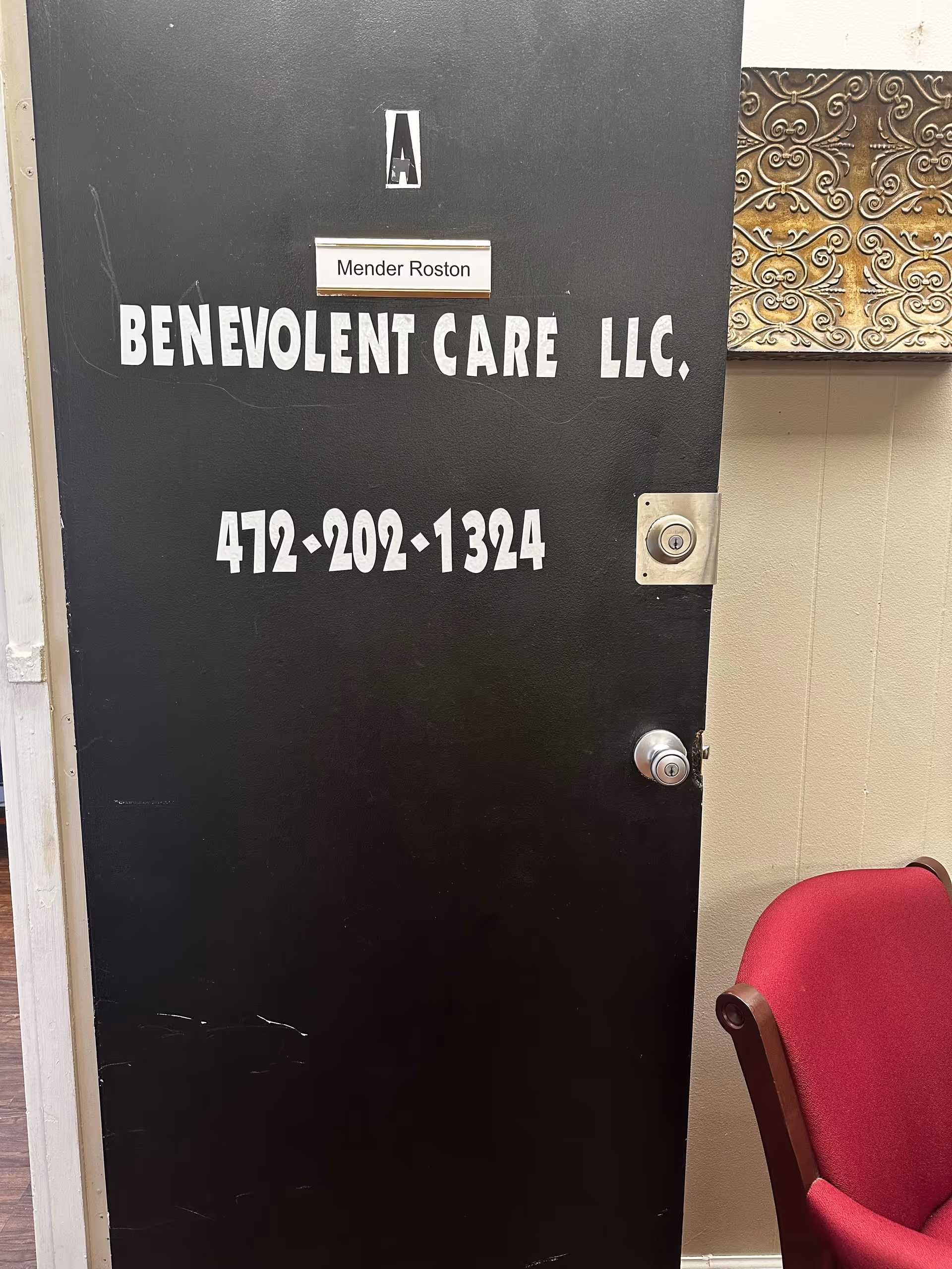 A black door with Benevolent Care LLC signage and a red chair nearby.