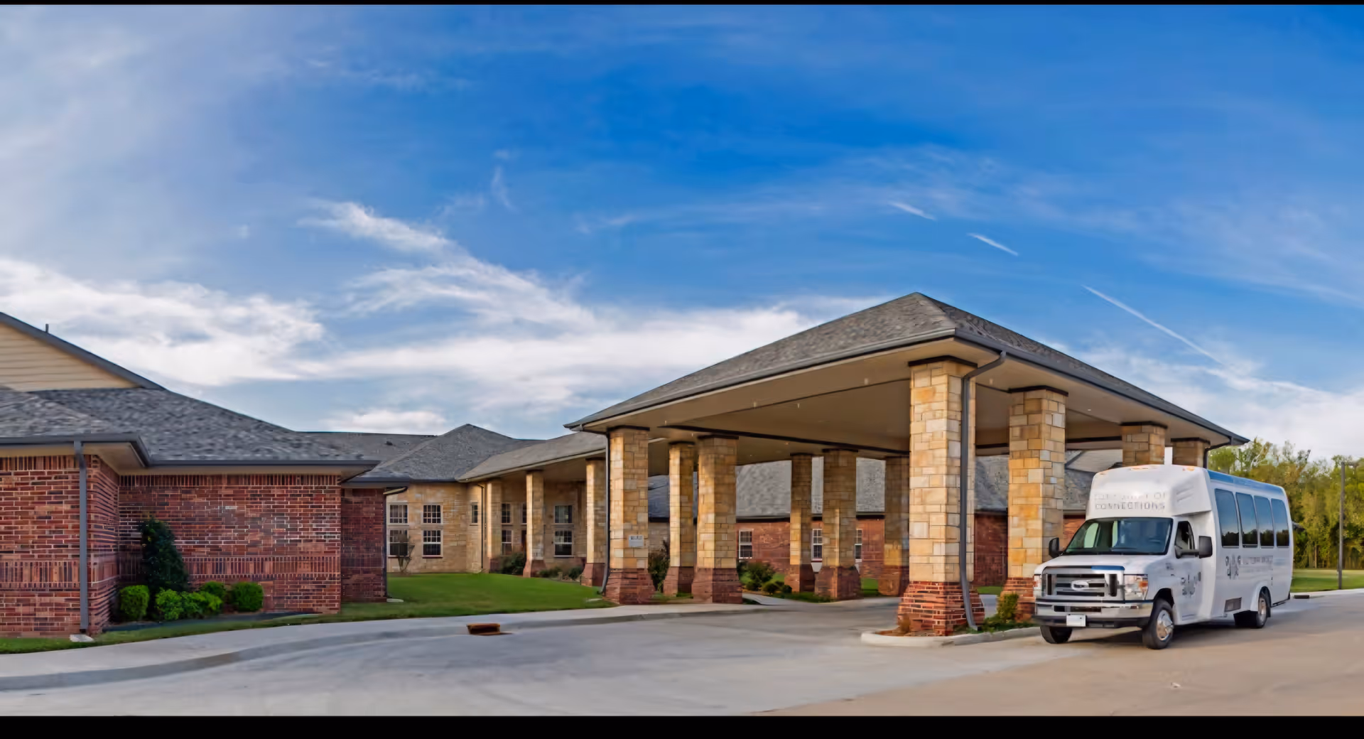 Brick senior care center with a covered entrance and a white shuttle bus.