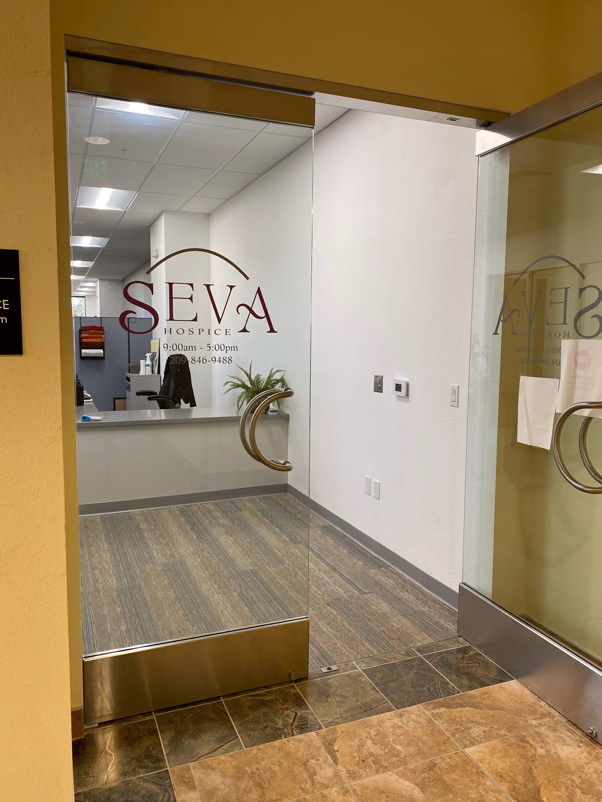 Glass entry doors display the Seva Hospice logo, opening to a reception area.