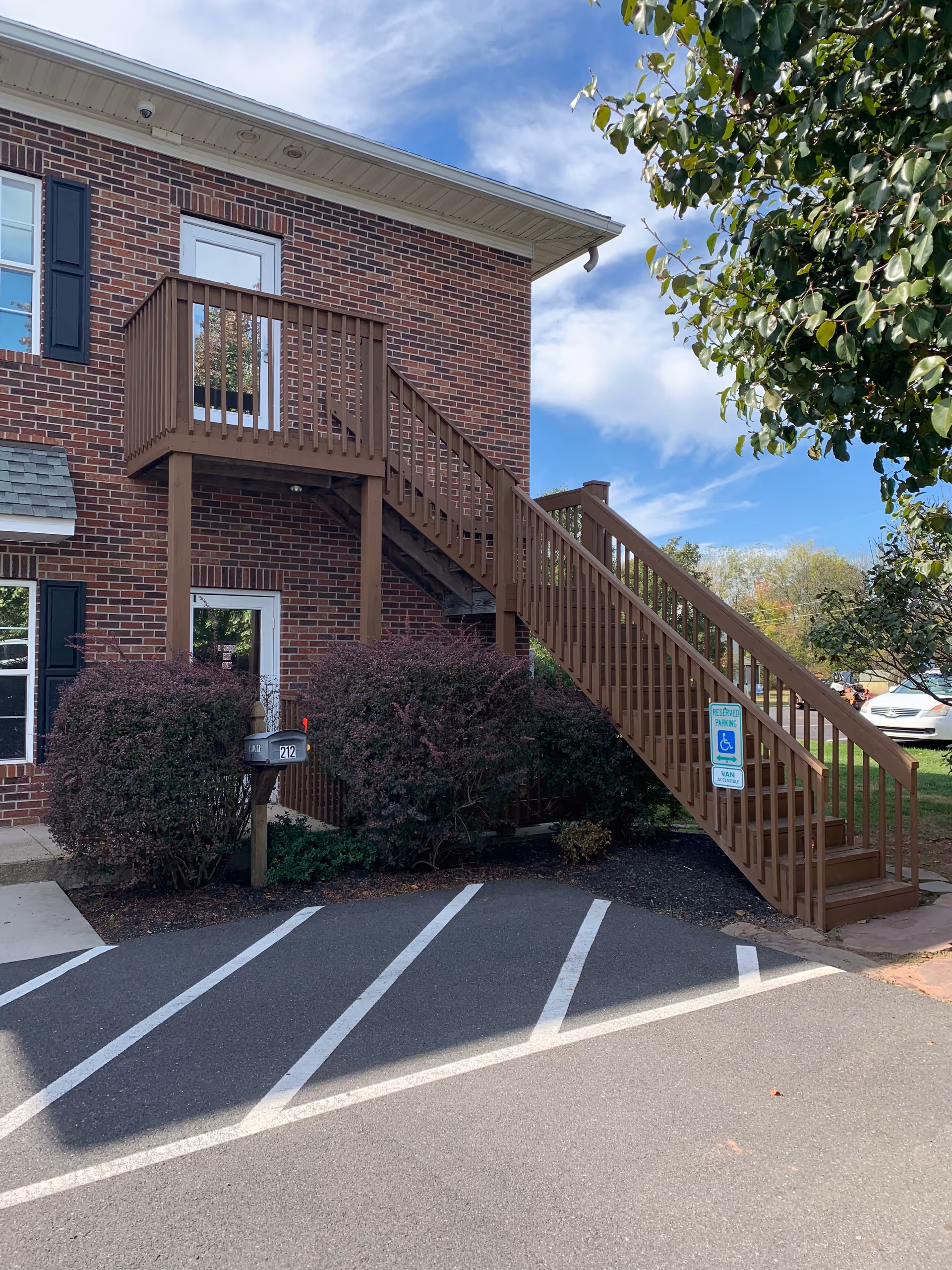 Exterior of a brick senior living building with a wooden staircase and parking.