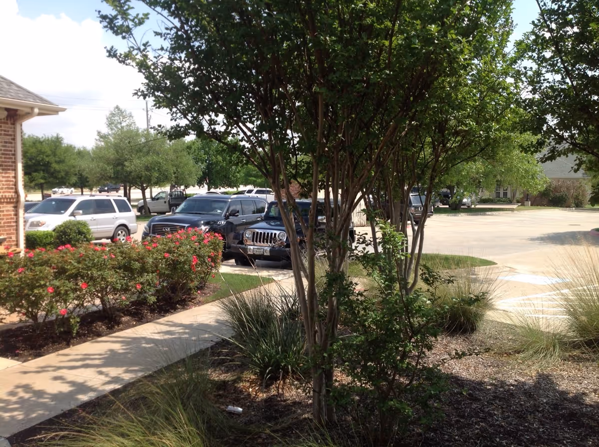 Exterior view of a brick building with a parking lot and landscaped shrubs.
