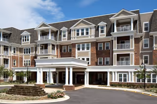 Front view of a multi-story brick senior living building with a paved circular driveway.