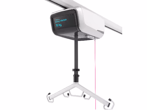 Ceiling-mounted patient lift with a hanging sling device in a clinical interior.