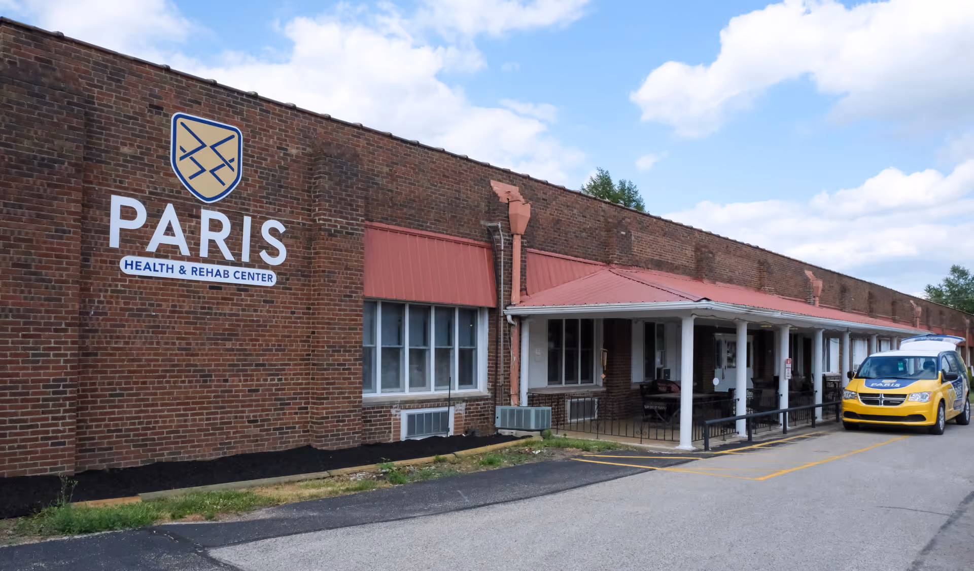 Brick exterior of Paris Health & Rehab Center showing the building's sign, a covered entrance with columns, and a parked yellow vehicle.
