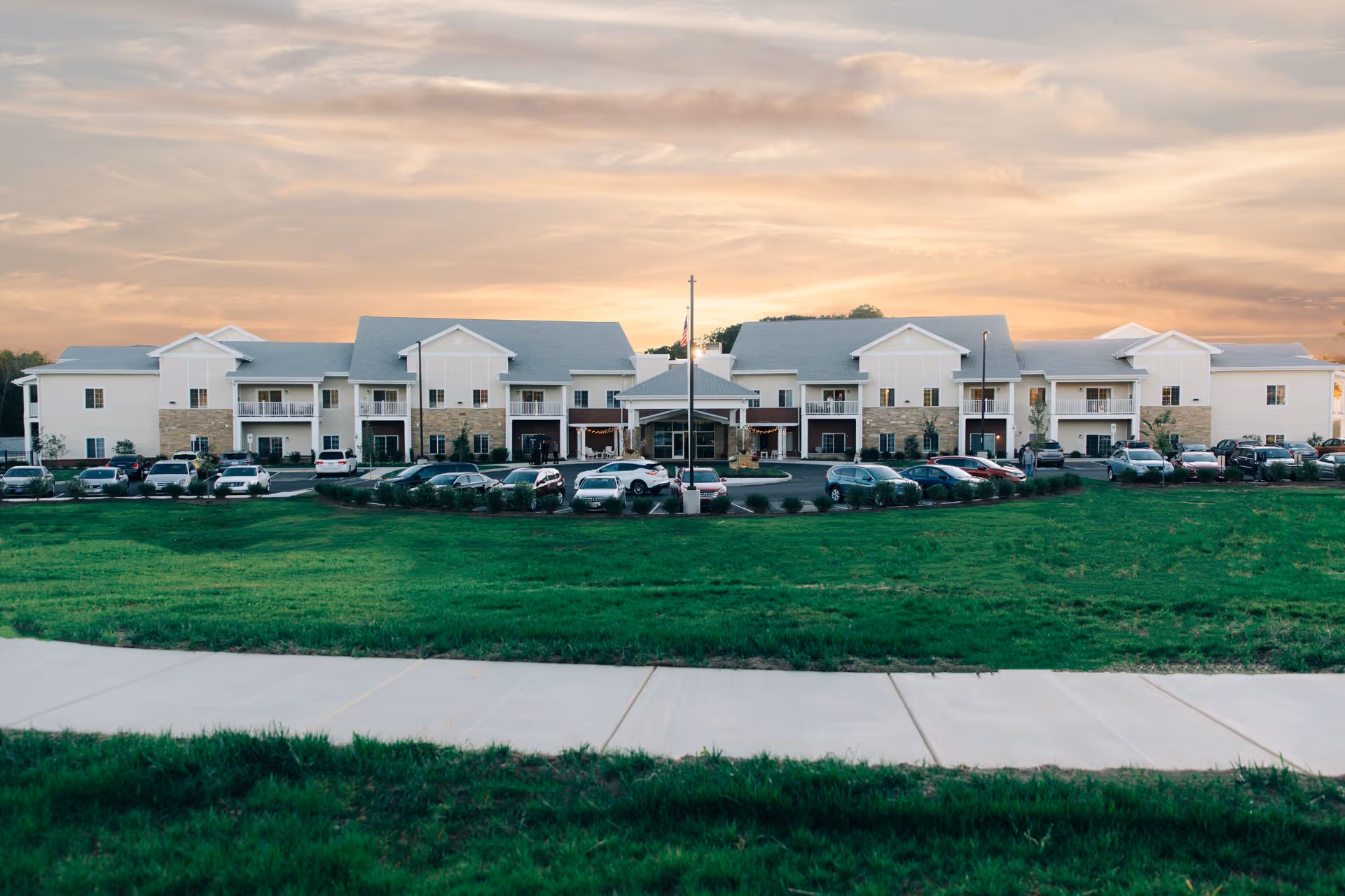 Sunset sky over a multi-unit senior living facility with parked cars and green lawn