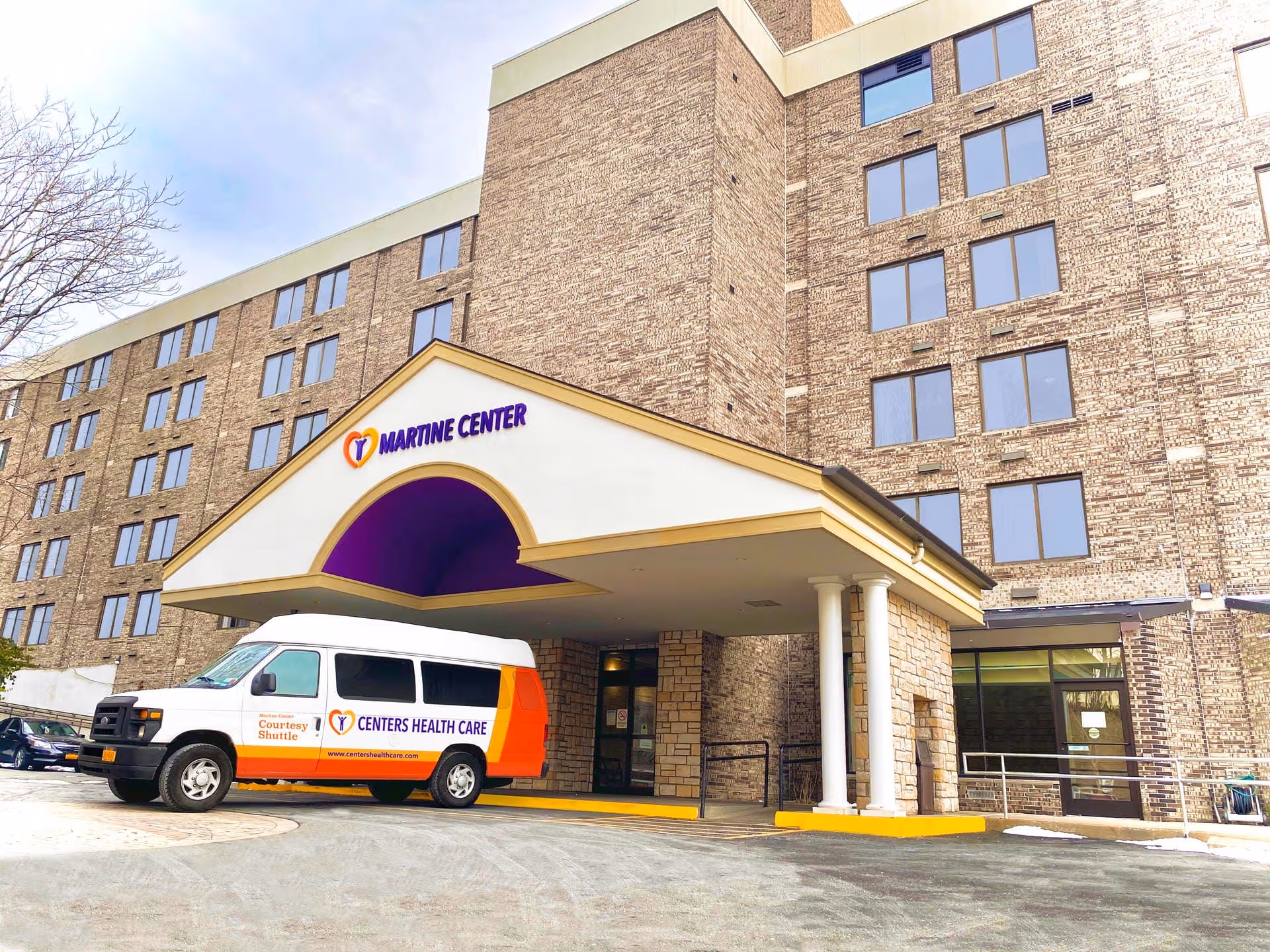 Exterior of a brick senior facility with a front entrance and shuttle van.
