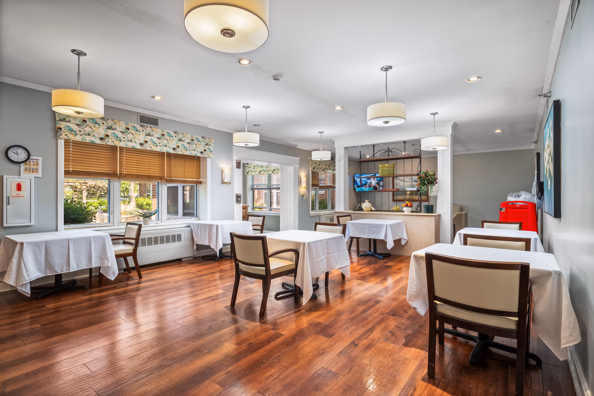 Dining room in Serenity Estates of Lincolnshire: tables with white cloths, wooden chairs, and windows.