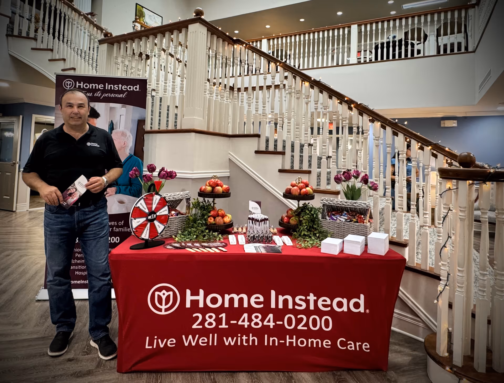 Front lobby area with a man beside a Home Instead promotional table near a staircase.