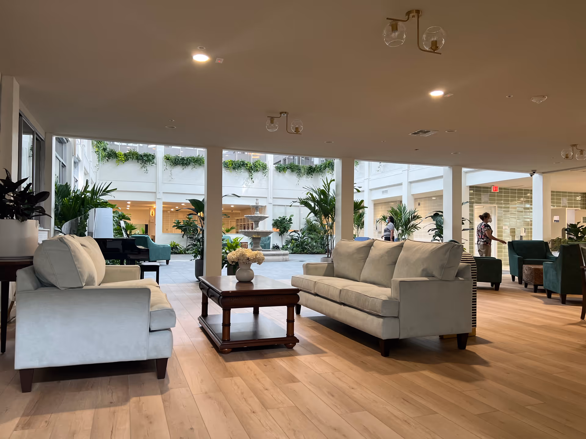 Spacious indoor lounge with sofas, plants, and a view of an airy courtyard through glass walls.