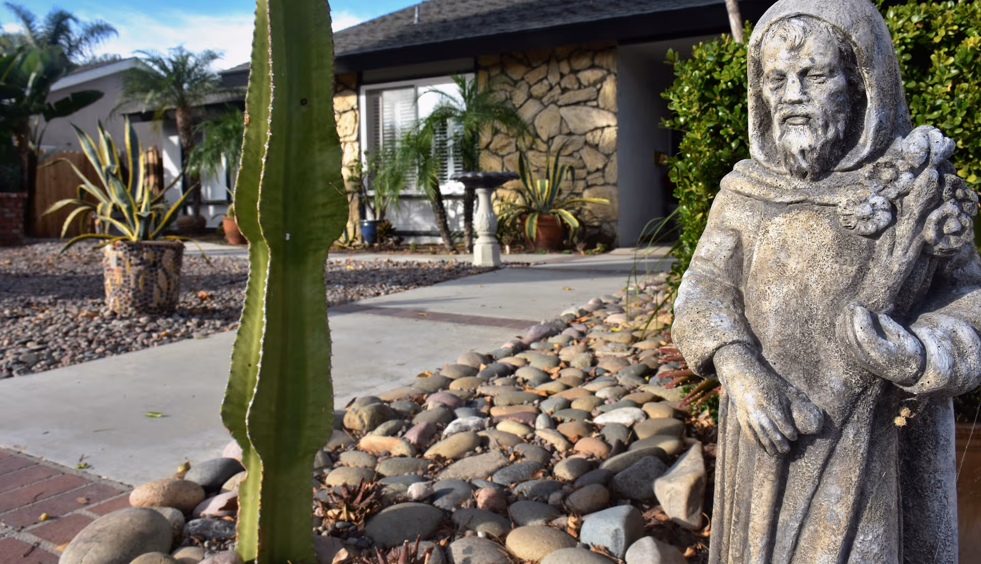 Front entrance of a stone building with desert landscaping, a large cactus, and a statue.