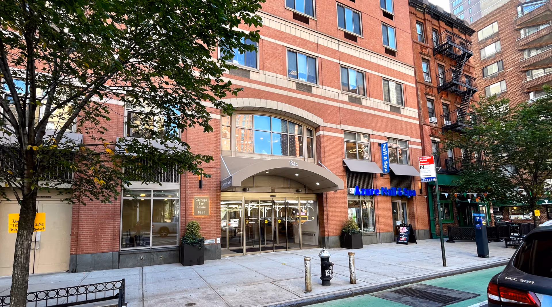 Street-level view of the red-brick Carnegie East House showing the awned main entrance at 1844, adjacent storefronts, and the sidewalk.