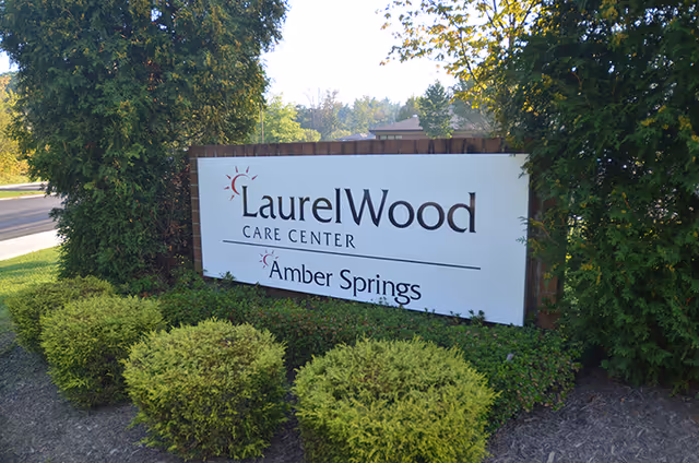 Outdoor sign reads LaurelWood Care Center Amber Springs, framed by shrubs.