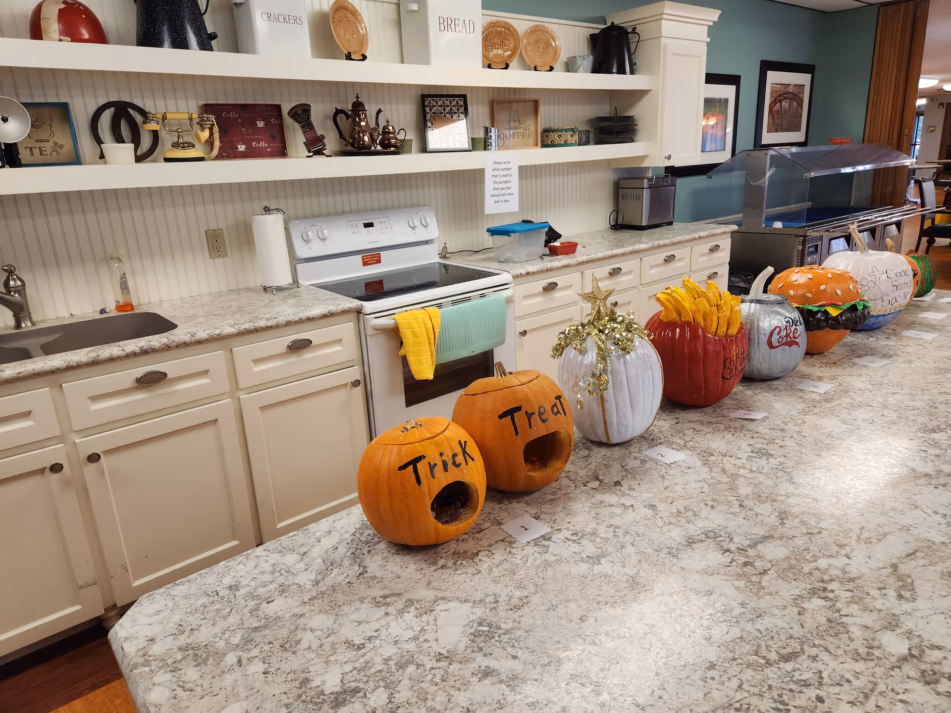 A kitchen counter with white cabinets, stovetop, shelves, and Halloween pumpkin decorations lined along the counter.