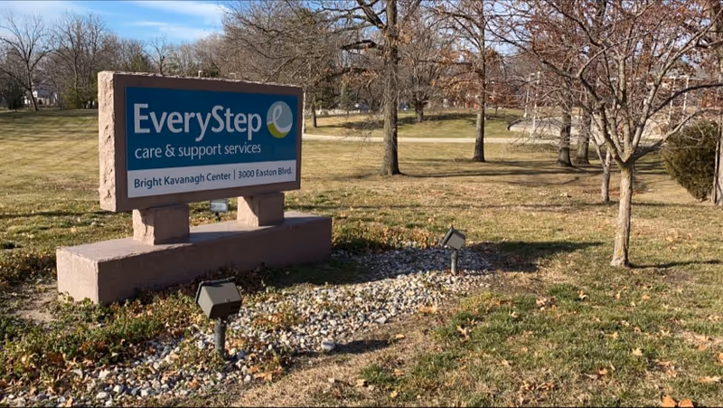 Outdoor scene featuring an EveryStep care sign on a stone base in a grassy park.