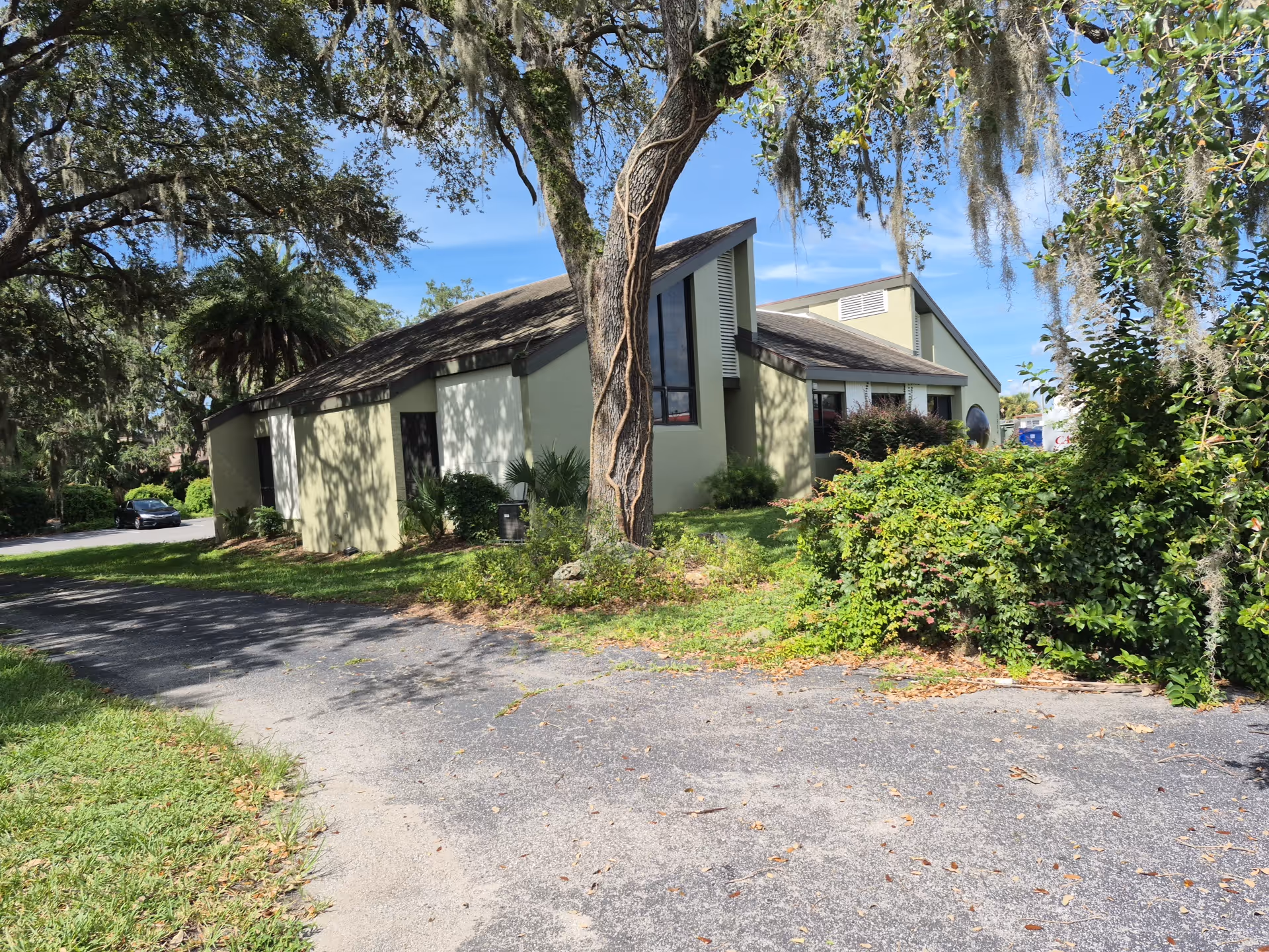 Single-story beige senior living building with trees, shrubs, and a gravel driveway.