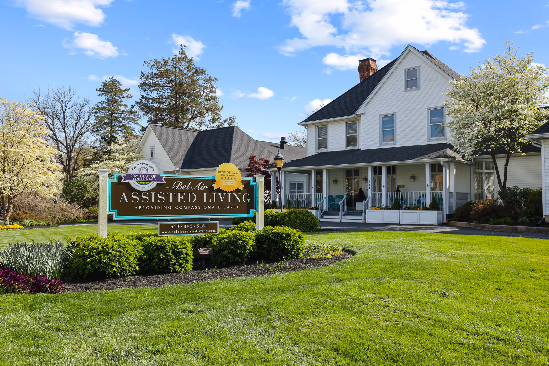 Front lawn and sign for Bel Air Assisted Living in front of a white two-story house with a porch.