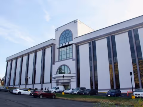 A modern front facade of a large building with tall windows and a parking lot.