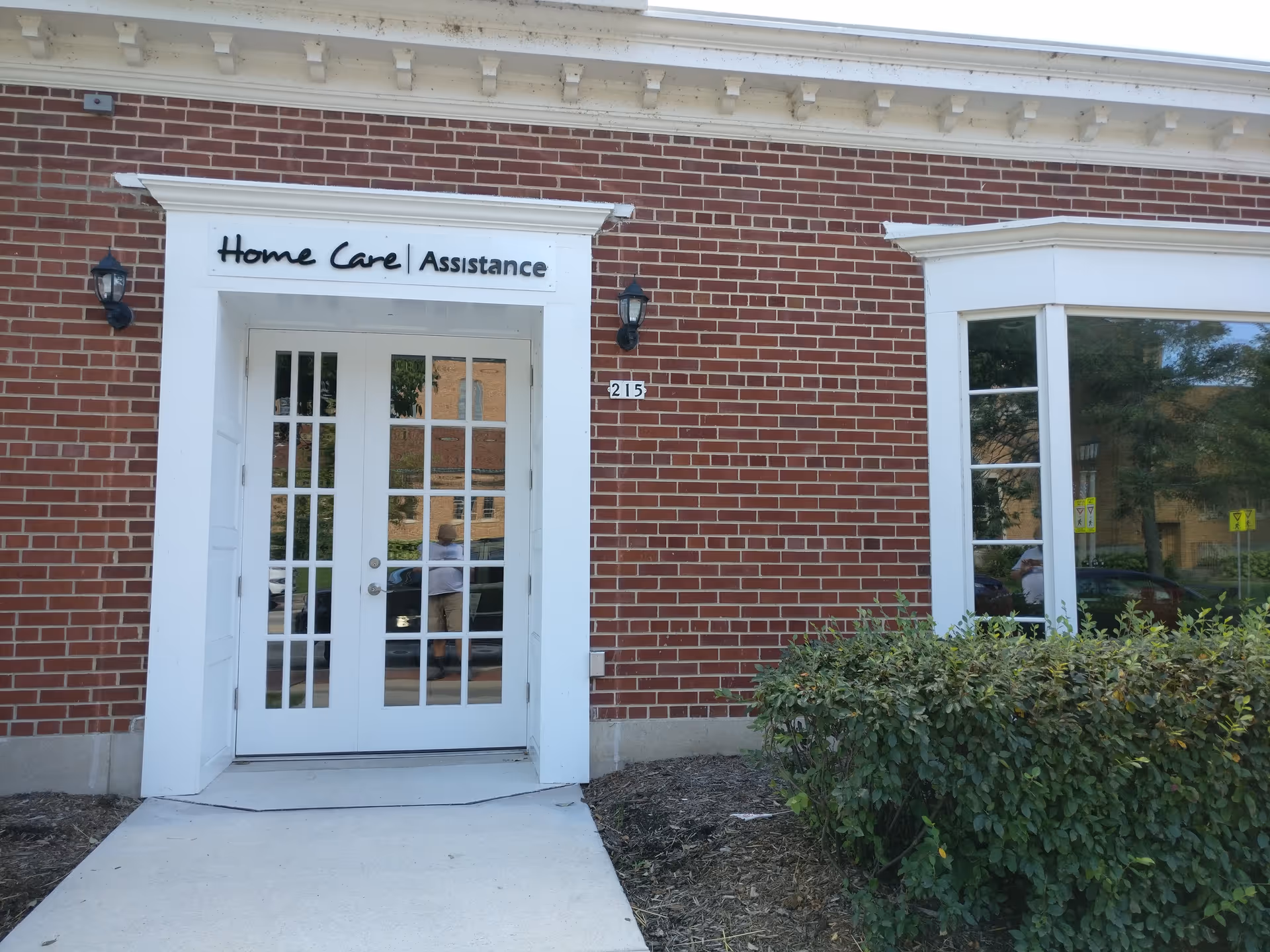 Brick building entrance with white double doors and a Home Care Assistance sign