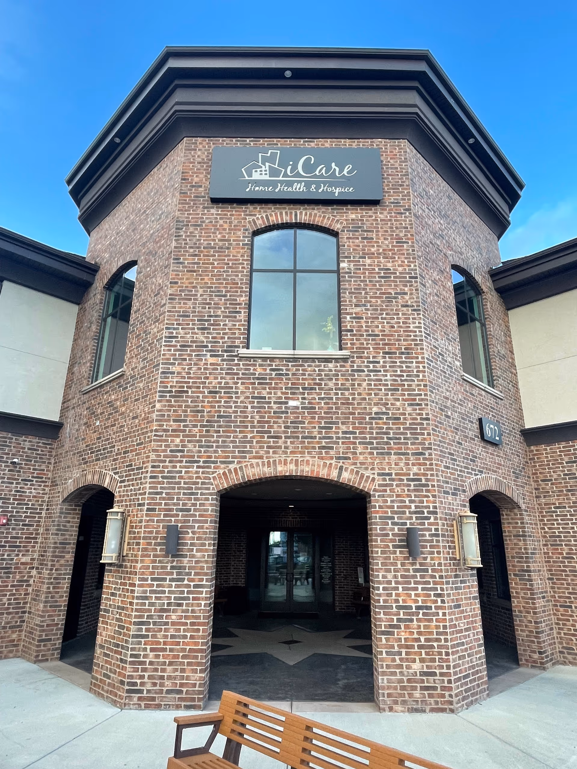 Brick building with iCare Home Health & Hospice sign and arched entrance under a blue sky.
