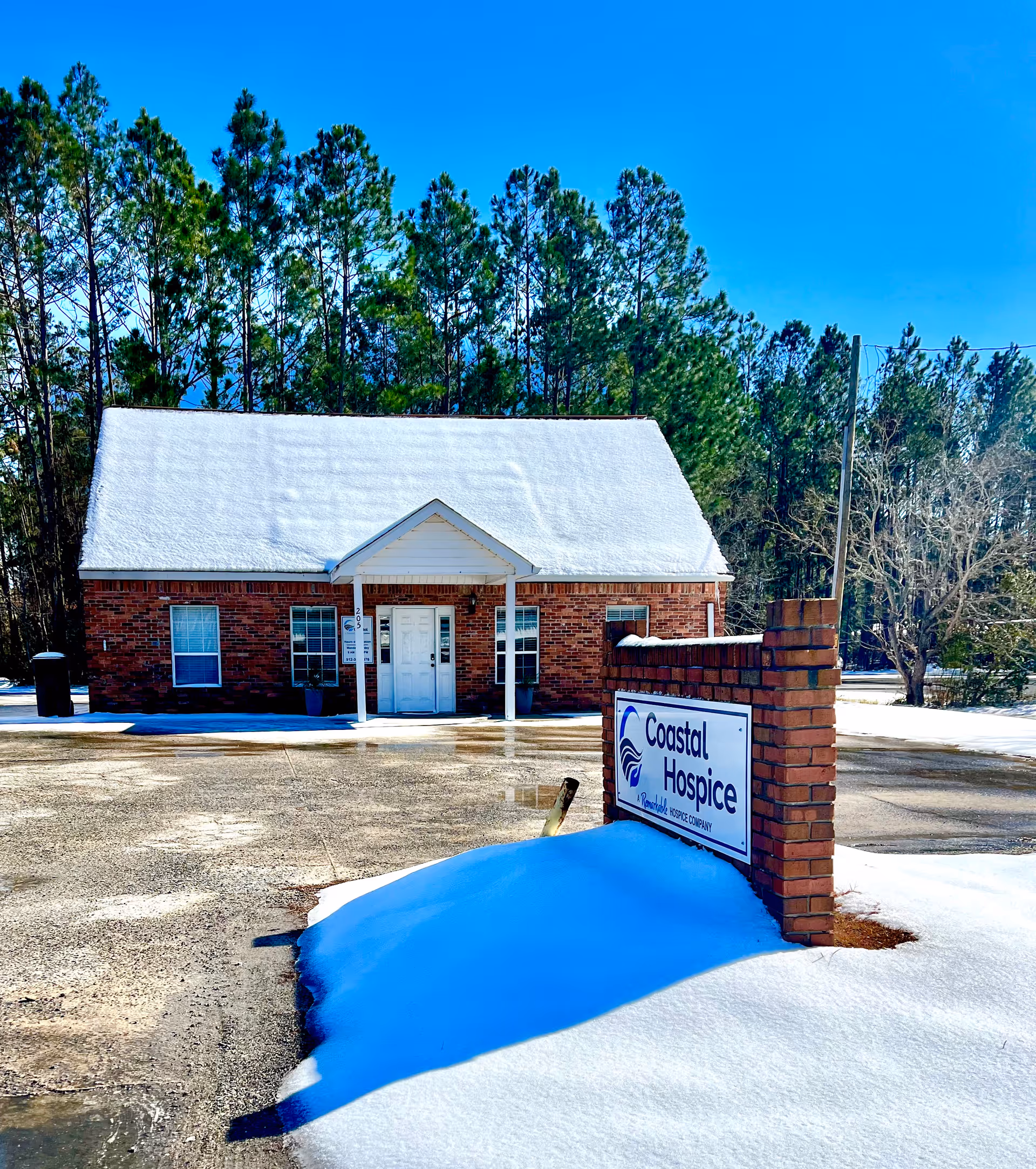 Snow covers the roof of a brick Coastal Hospice building with a sign at the entrance.