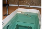 Accessible indoor spa tub with handrails and seating inside a facility bathroom.