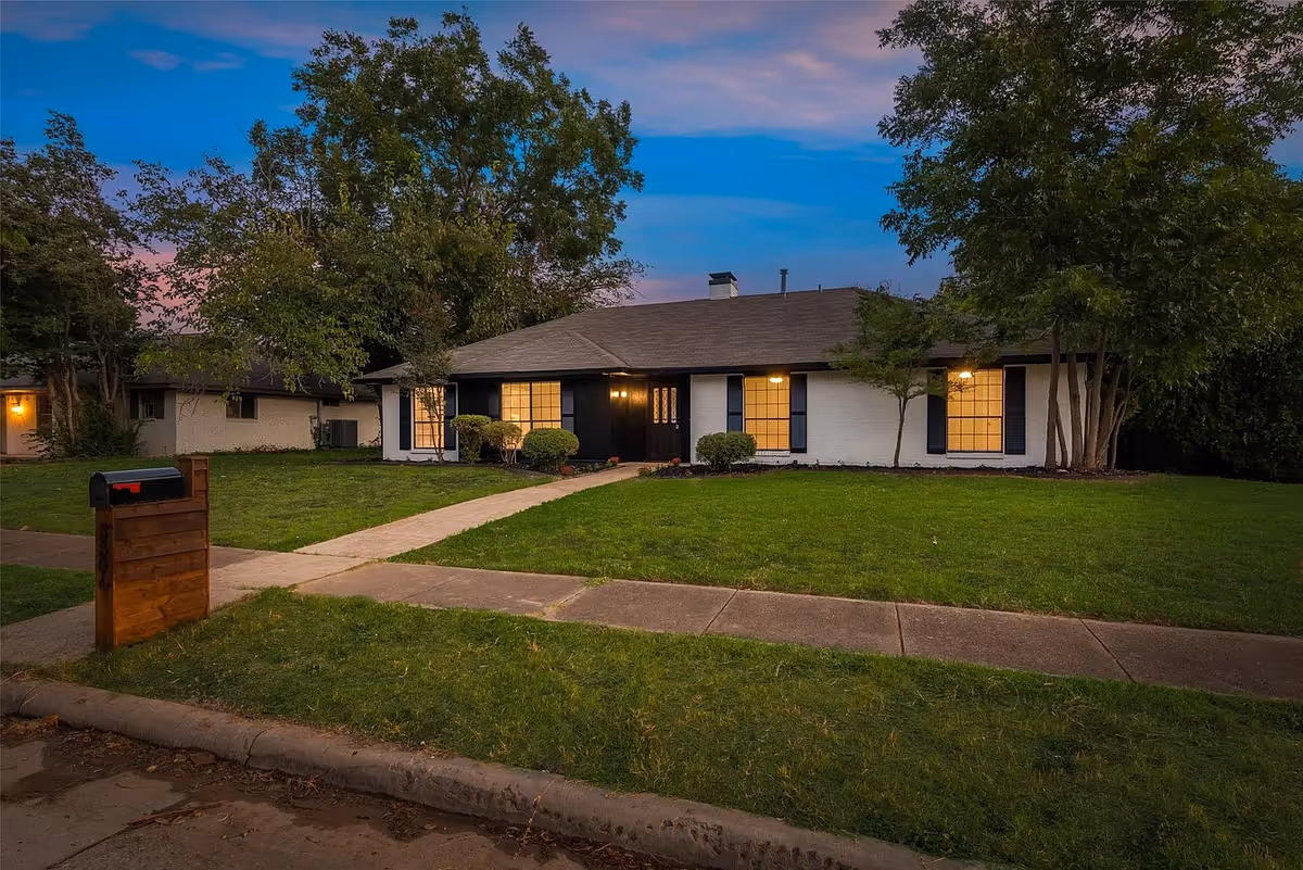 Single-story senior living facility with a manicured lawn, walkway, and lit front entrance.
