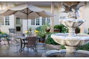Outdoor patio with tables, chairs, umbrellas, plants, and a fountain beside the building.
