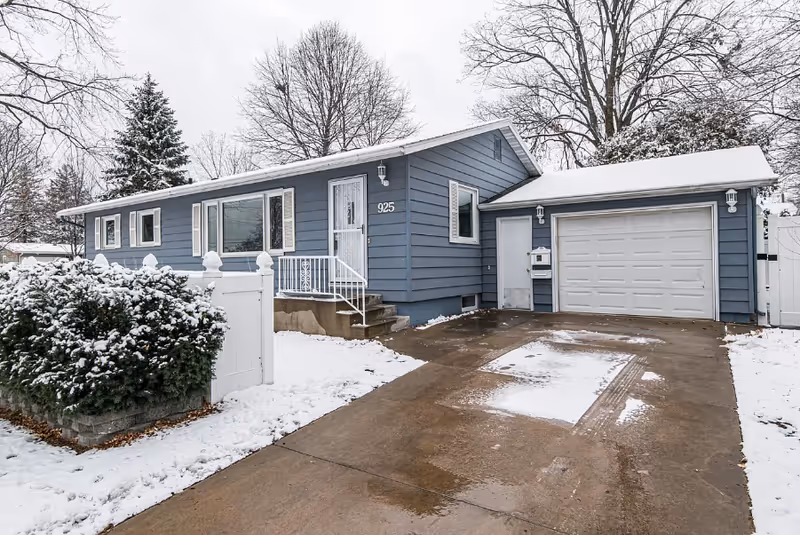 Blue, single-story home exterior with snow, driveway, and attached two-car garage.
