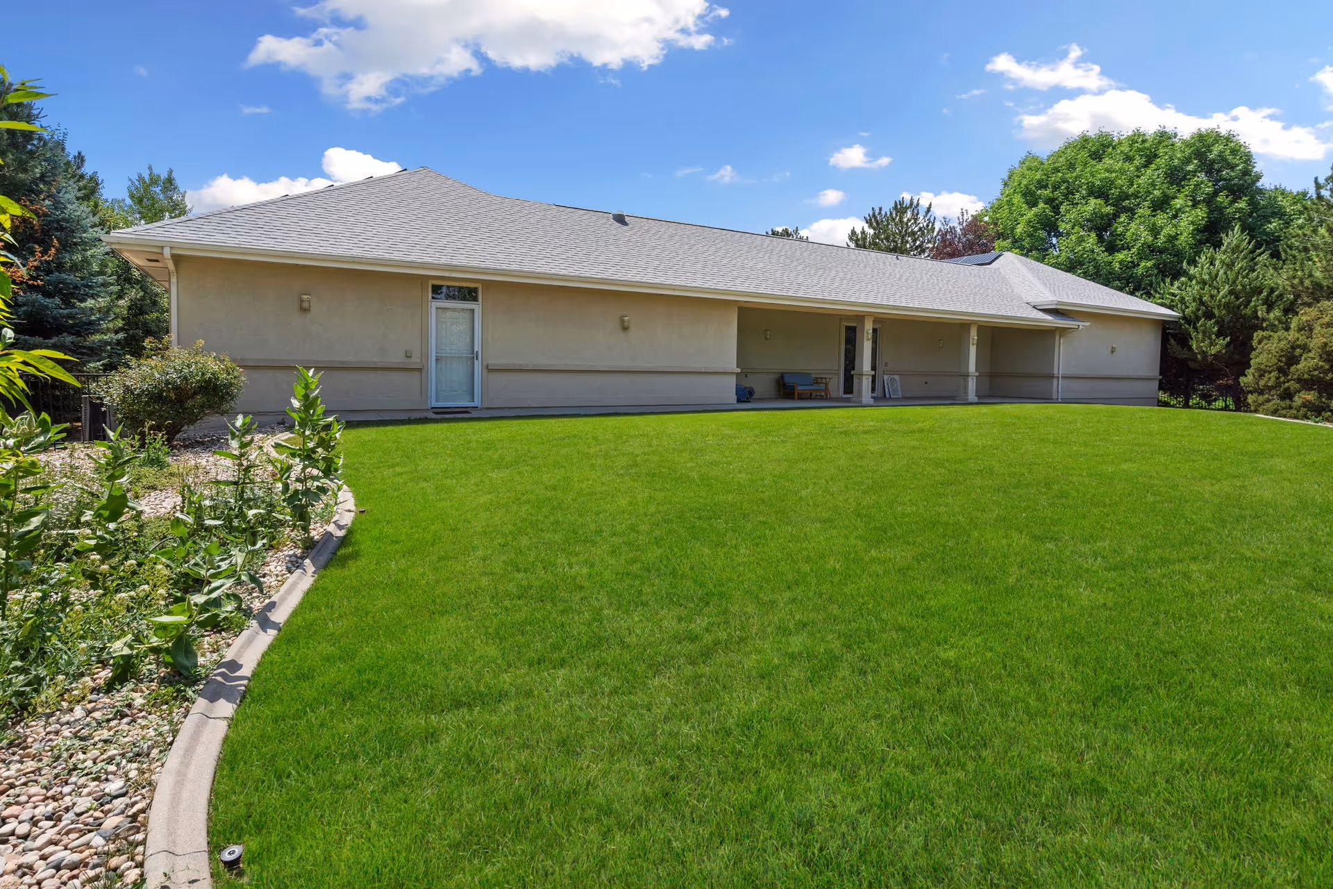 Single-story beige building with a large green lawn, covered porch, and outdoor seating.