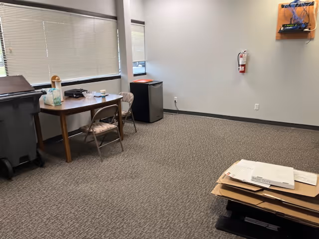 Interior room with a table, folding chairs, trash can, and stacks of papers.