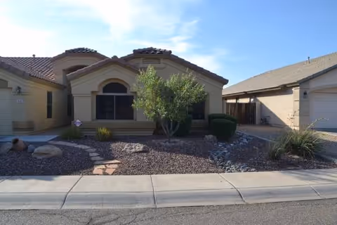 Front view of a single-story residential building with desert landscaping and a walkway.