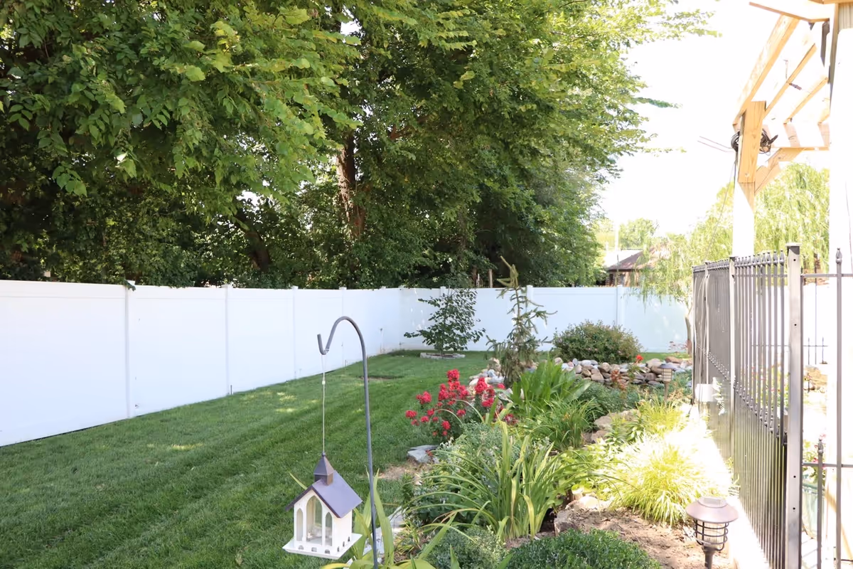 Lush backyard garden with a white fence, colorful flowers, and a hanging birdhouse.