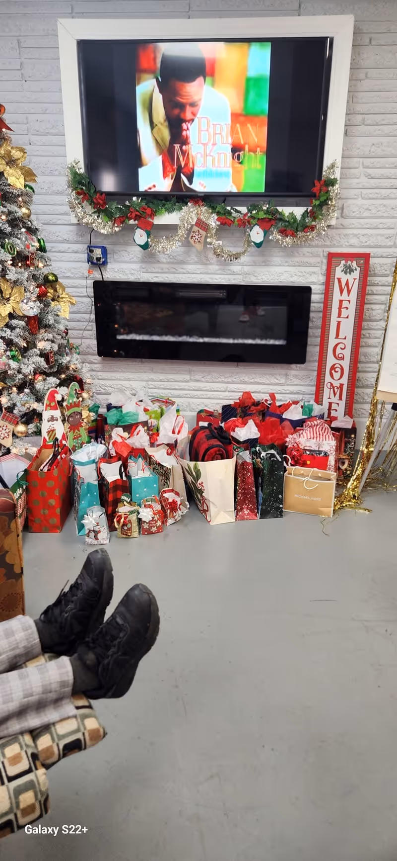 Holiday setup in a facility lounge with a TV, garland, gift bags, and a welcome sign.