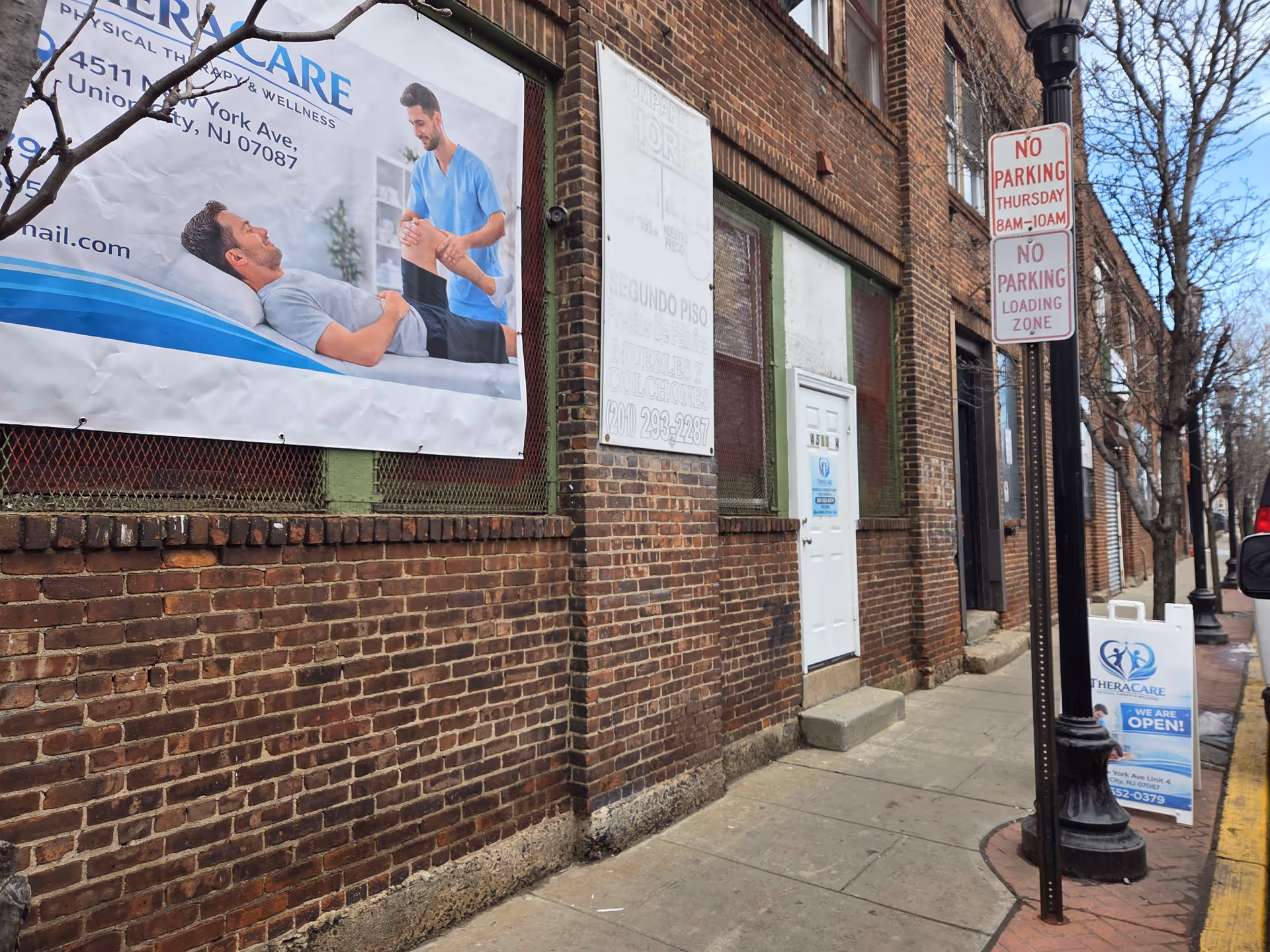 Brick exterior of TheraCare Physical Therapy and Wellness with banners and a sidewalk.
