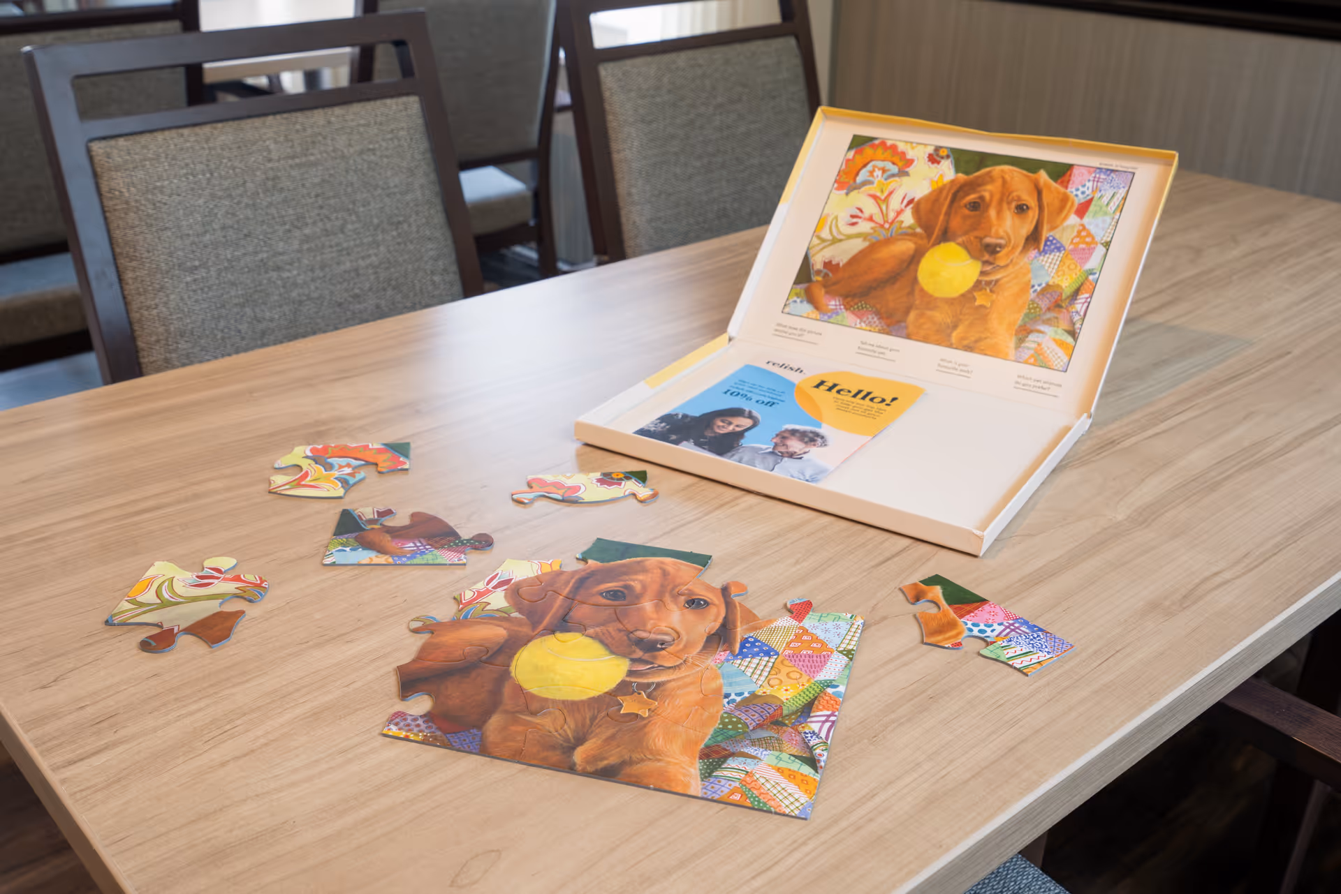 Puzzle pieces and a dog-themed board game on a wooden table in an interior lounge.