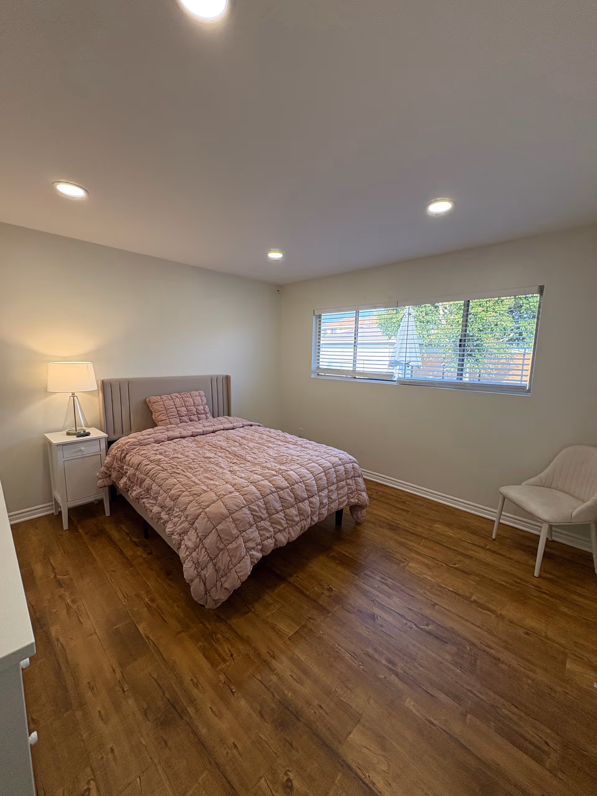 Bedroom in a senior living facility with a pink quilted bed and window.