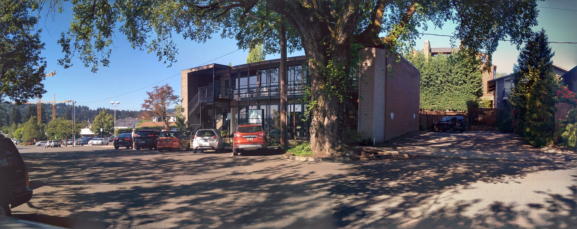 Exterior shot of Seasons Living facility with parked cars and a large tree.