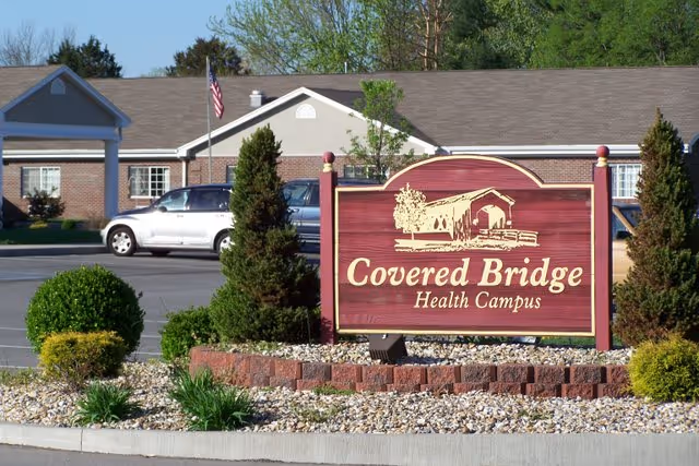 Front view of Covered Bridge Health Campus sign with landscaping and a brick building behind.