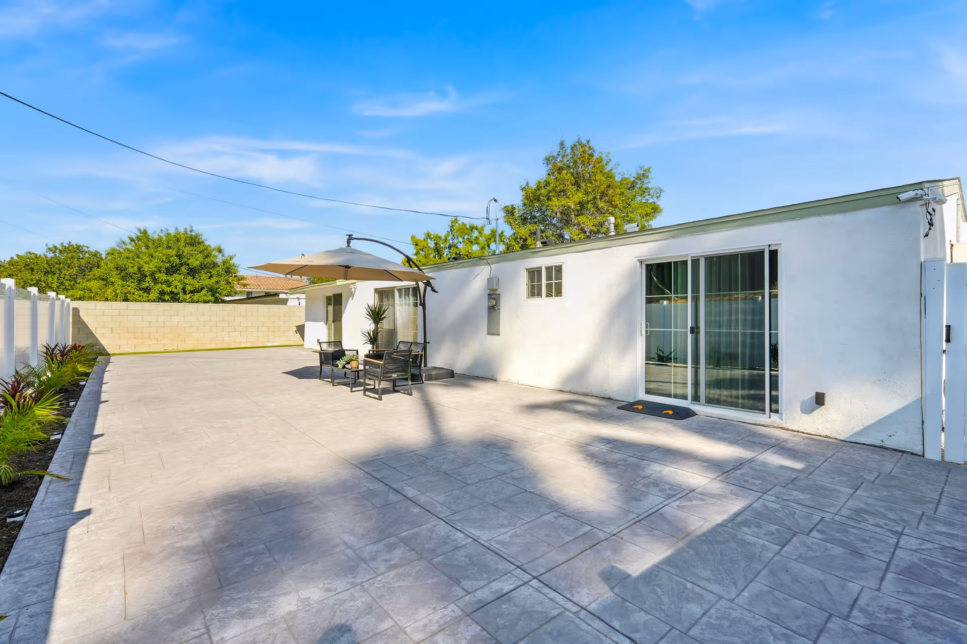Sunny outdoor patio with umbrella, seating, and sliding glass door on white building.