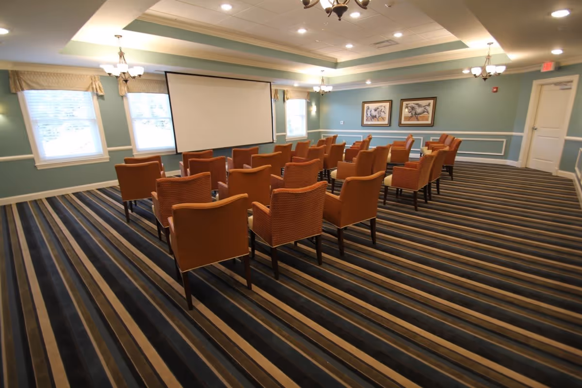 A carpeted meeting room with rows of orange chairs arranged facing a projection screen.