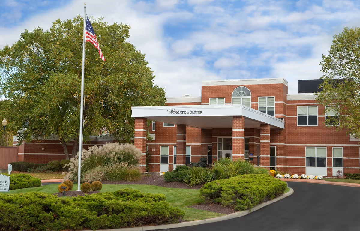 Brick senior living facility exterior with entrance canopy, flagpole, and manicured landscaping.