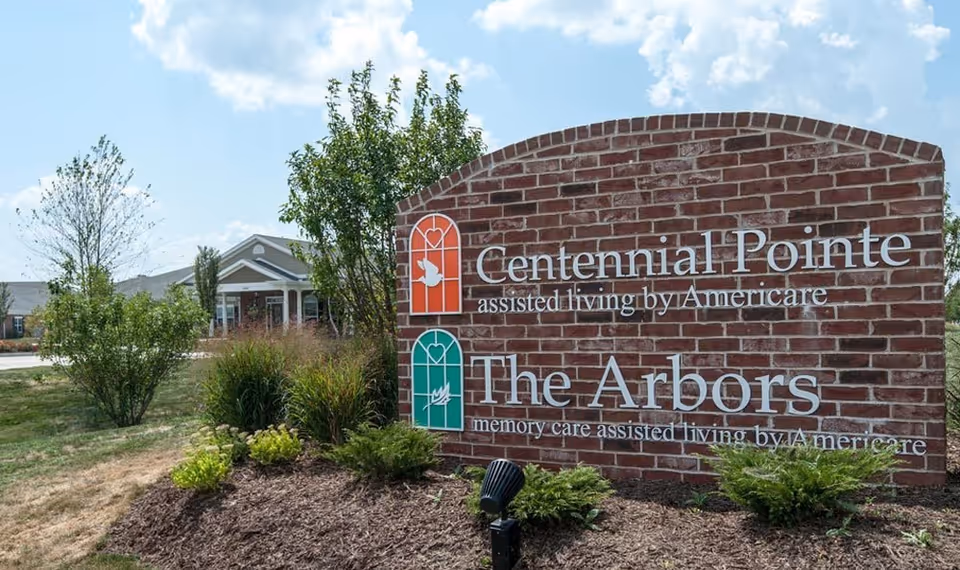 Brick sign reading Centennial Pointe and The Arbors, with landscaping and a building in background.