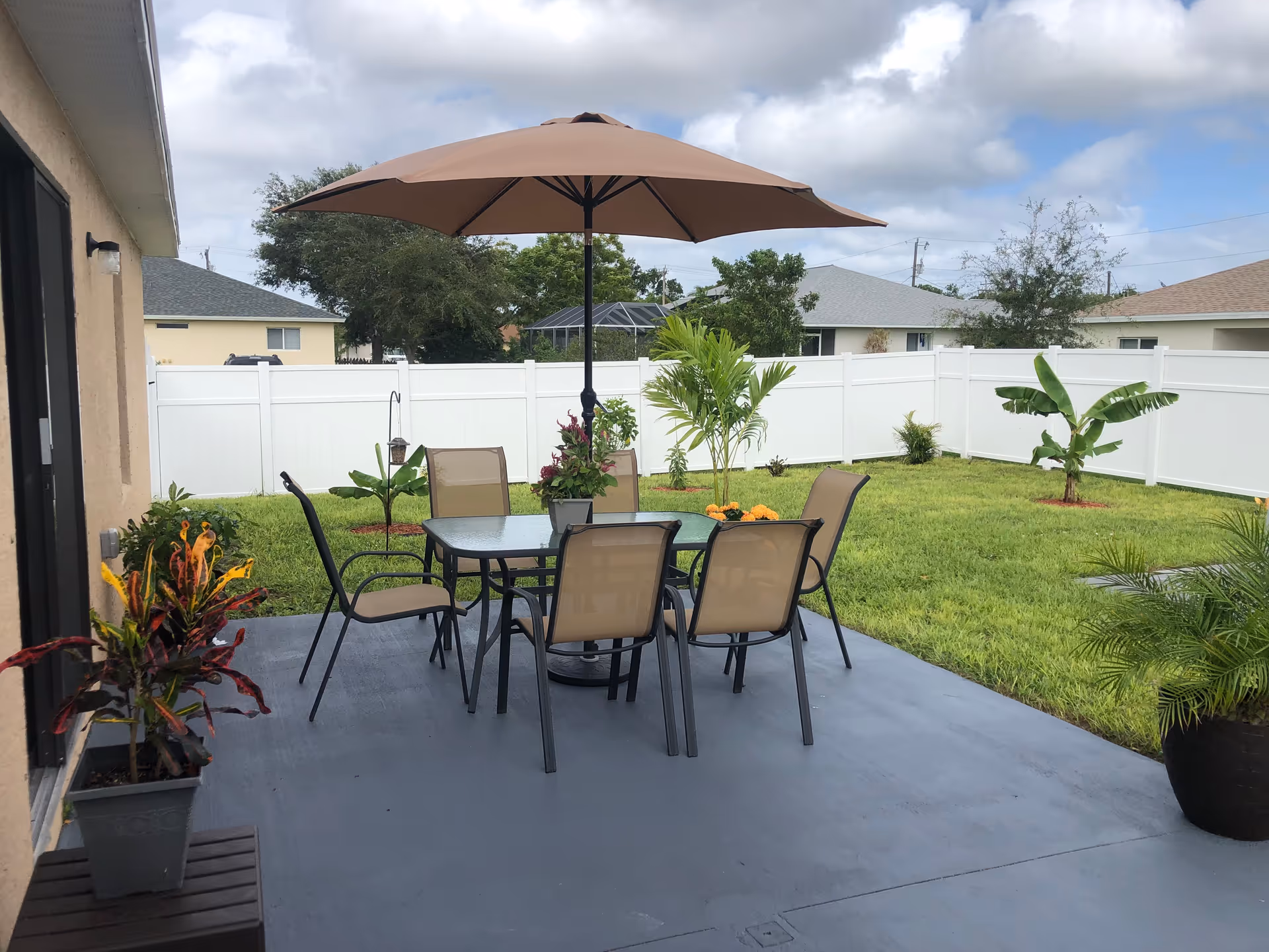 Outdoor patio with umbrella, table, and chairs in a fenced backyard.