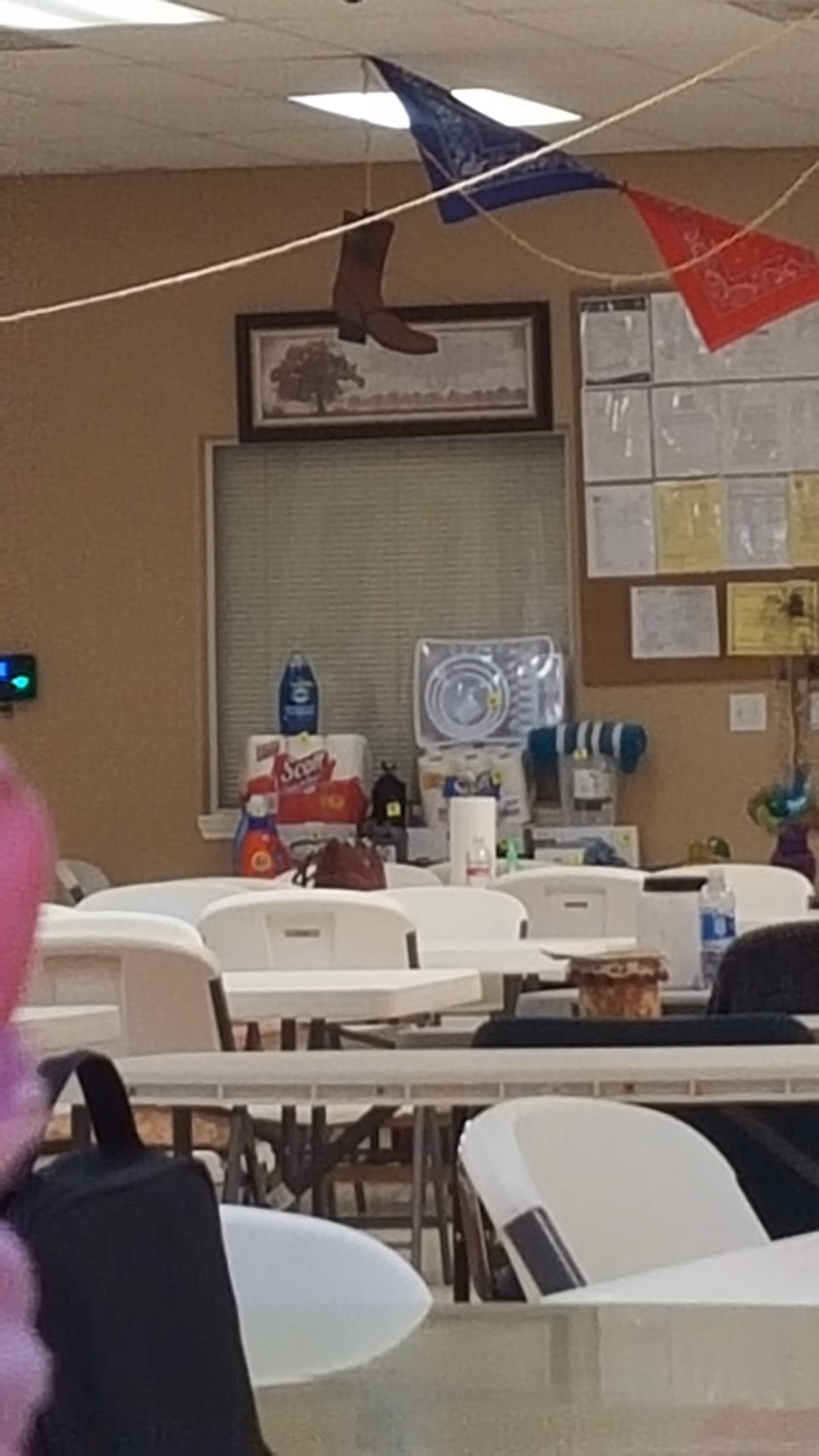Indoor dining hall with white tables and chairs, supplies on counters, bunting overhead.