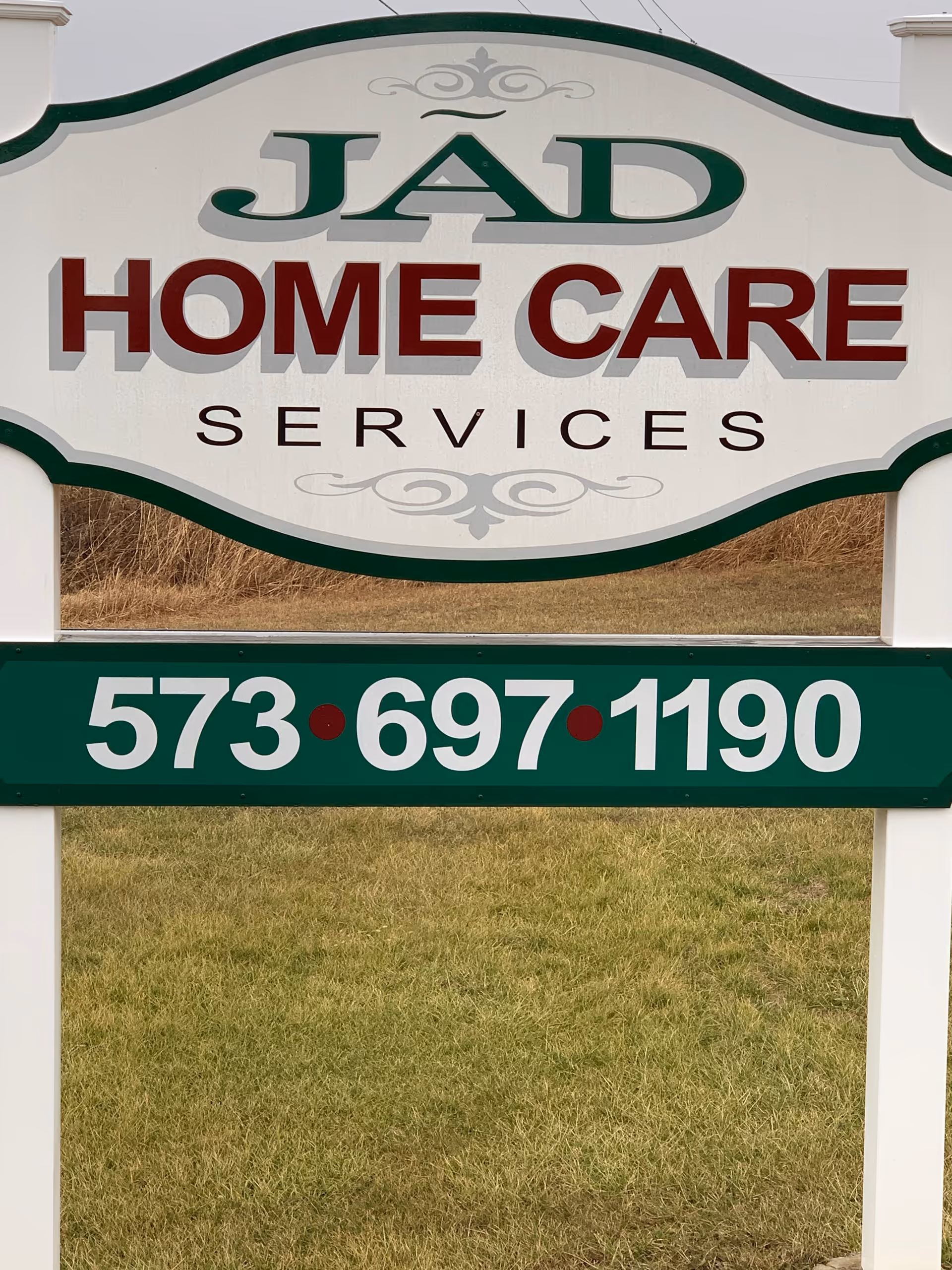 Outdoor sign displays JAD HOME CARE SERVICES with phone number and grassy background.