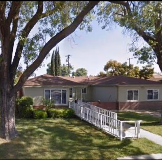 Single-story senior living facility with ramp entrance, lawn, and trees.