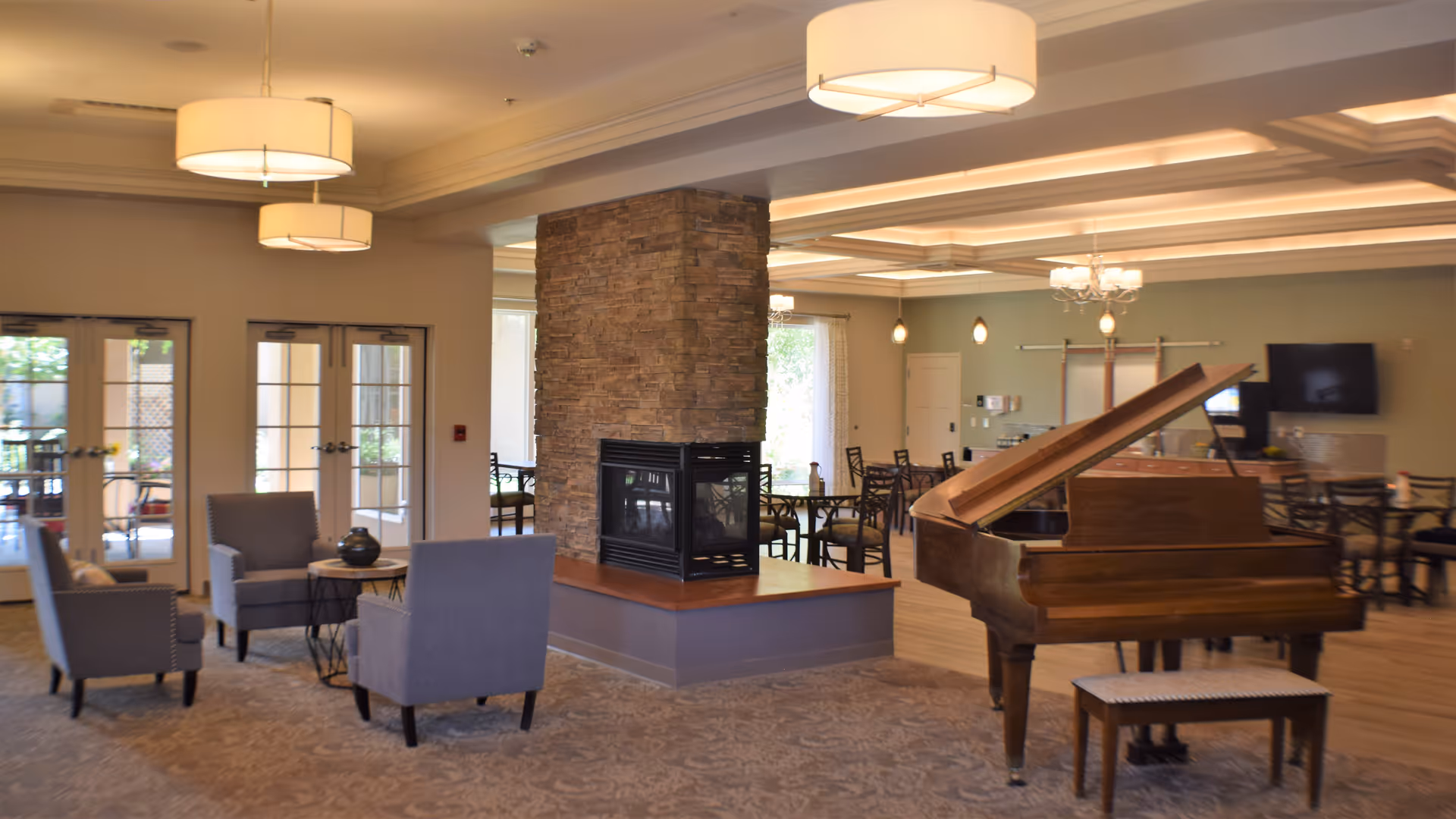 Bright lounge area with a stone fireplace, grand piano, and seating in a spacious interior.
