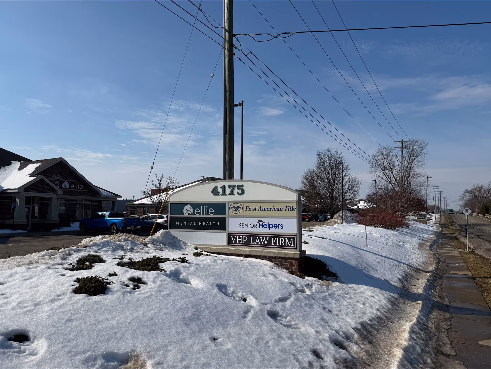 Outdoor street scene with a multi-tenant sign including Senior Helpers, snow on ground.